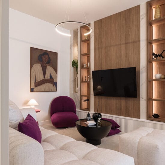 Living room with beige tufted sectional, purple cushions, and a round black coffee table in front of a TV wall unit.